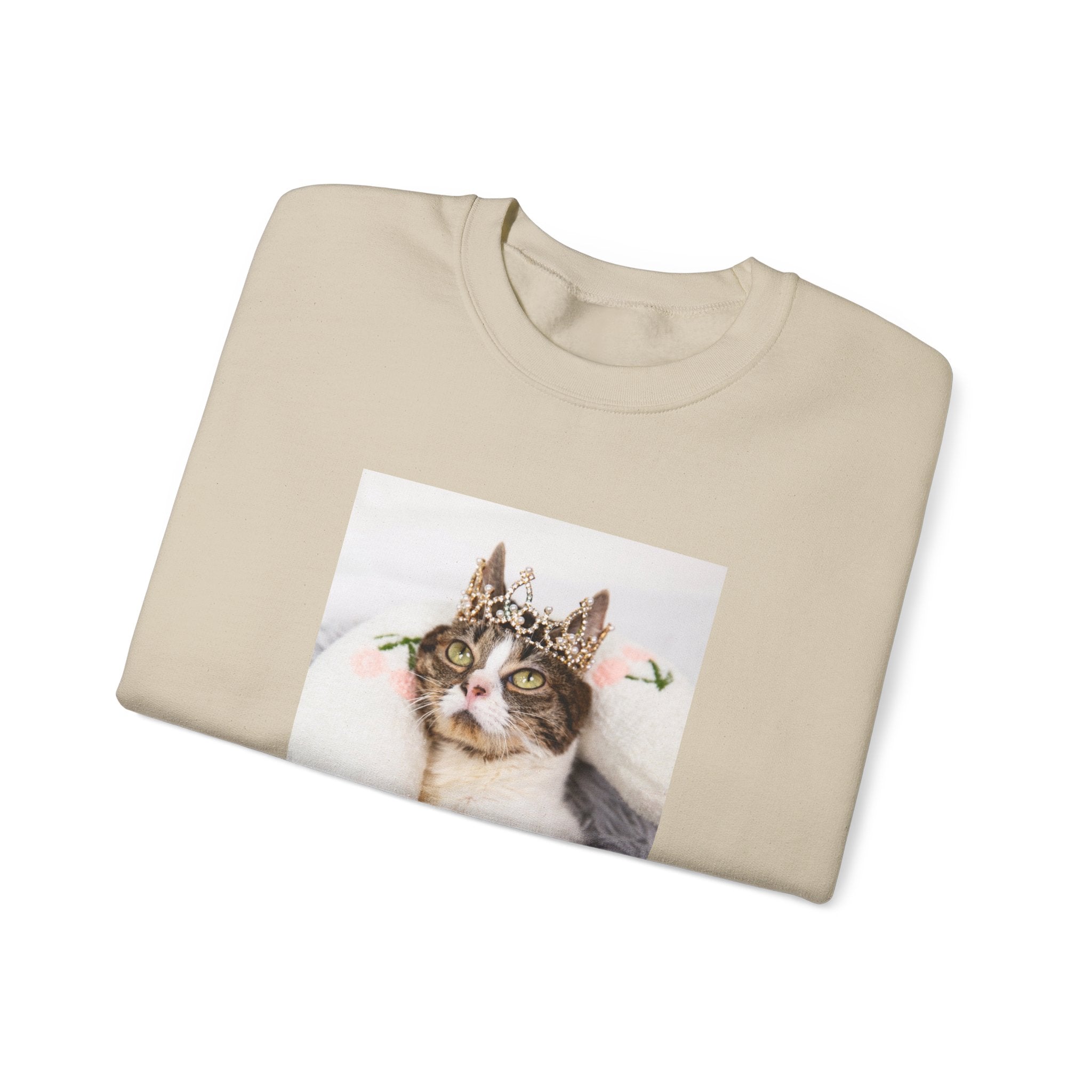 Folded beige sweatshirt with a cat wearing a crown graphic on a white background